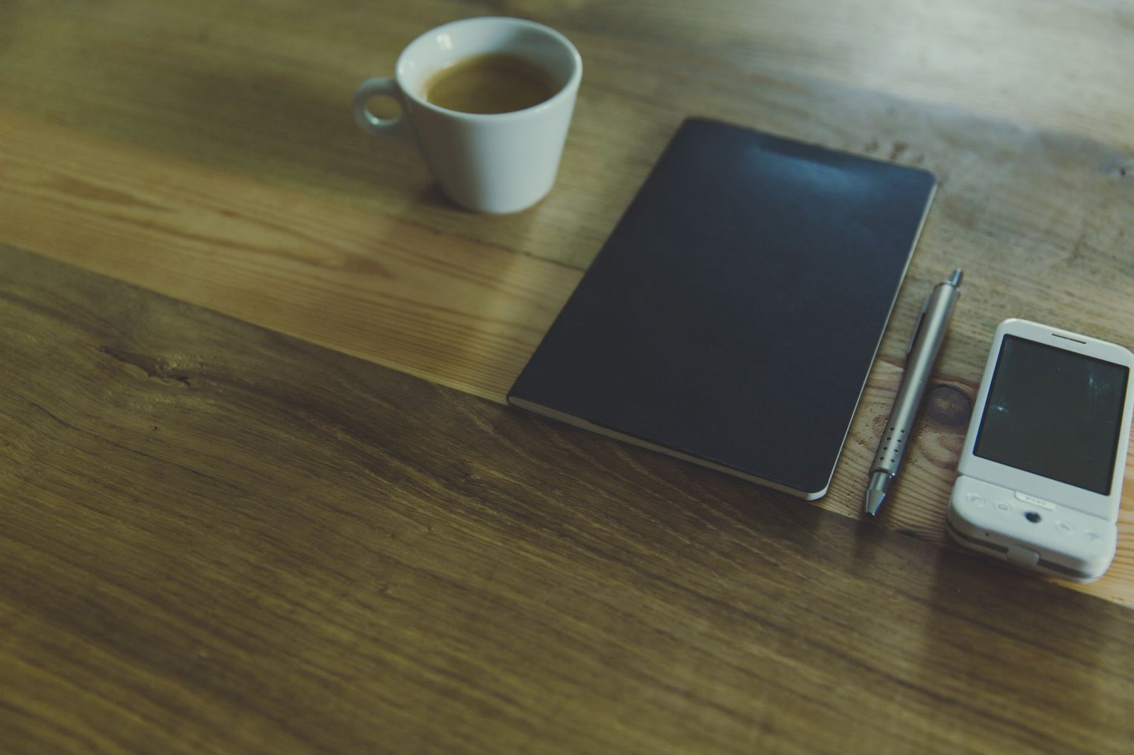 A tablet, a phone, a pen and a cup of coffee on a wooden desk